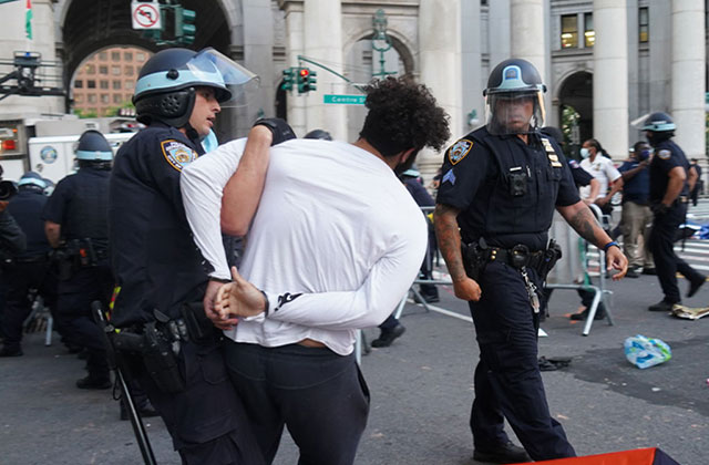 Police Force. Police officer in uniform arresting a Black man with curly hair, white shirt and black pants at a protest.