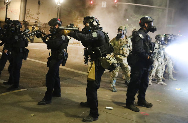federal officers point large black weapons at protesters