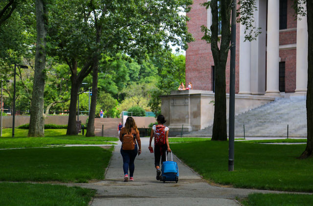 two people with luggage walk through a college campus.