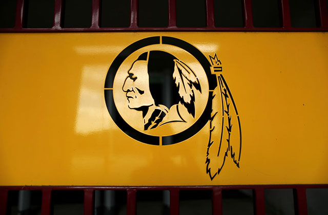 Washington DC NFL Team. Logo with yellow background and black ink of a stereotypical image of a Native American man wearing head feathers.