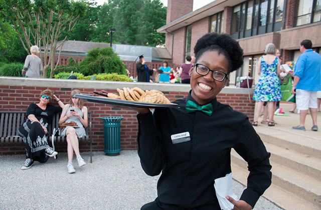 Black Waitress. Young Black woman with a dark Afro wearing a green bow tie and black shirt and pants holding a platter of cookies.