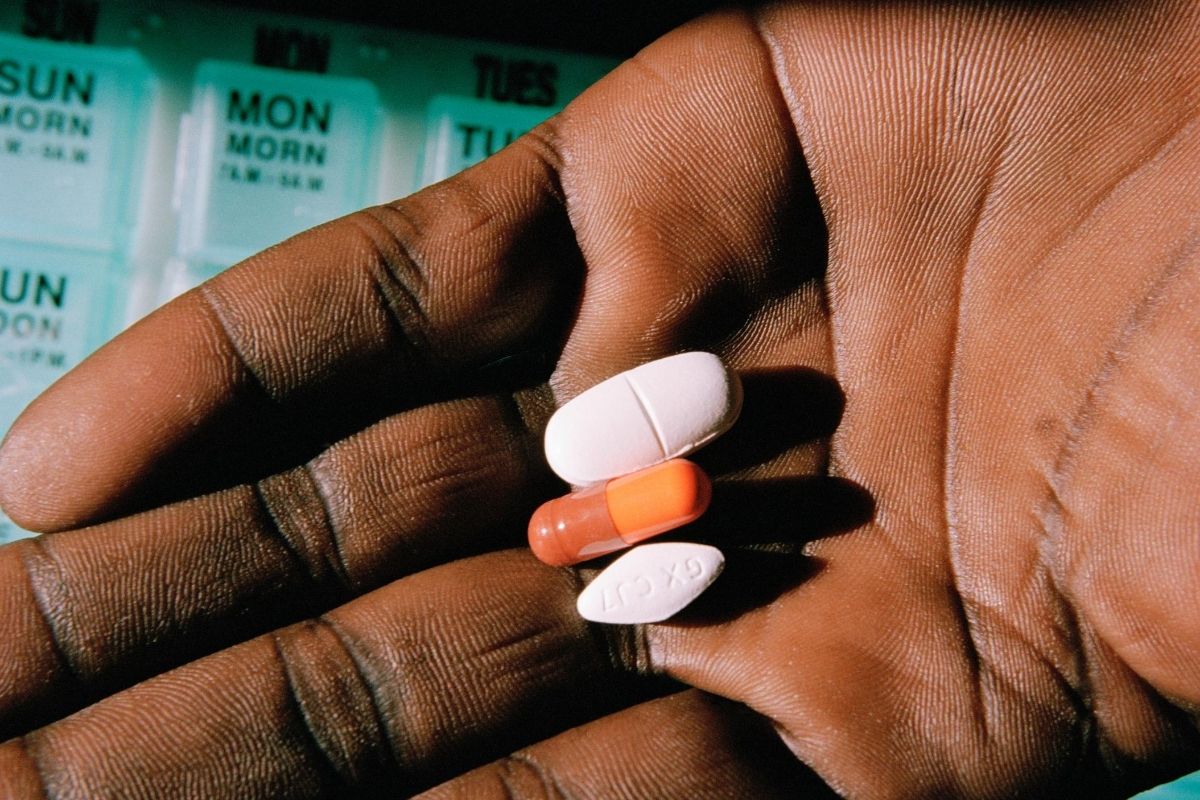 A Black hand palm facing up with three pills, a white oblong pill, an orange capsule and a white diamond shaped pill
