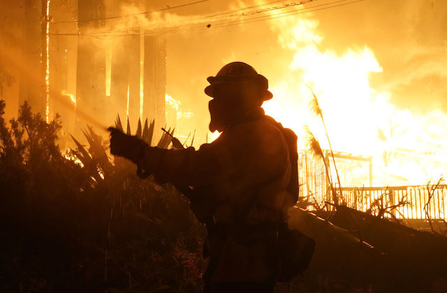 The shadow of a firefighter can be seen in the forefront as a fire rages in the background.