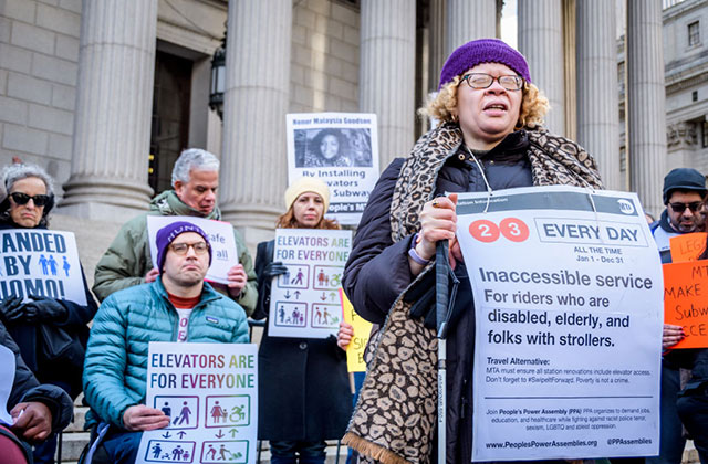 Disability Justice. A group of protestors standing outside of a court house hold signs calling for better access to the subway.