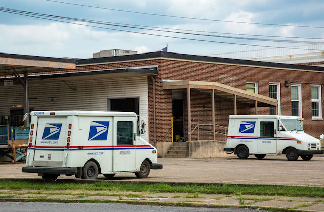 Two mail trucks are parked in an otherwise empty parking lot.