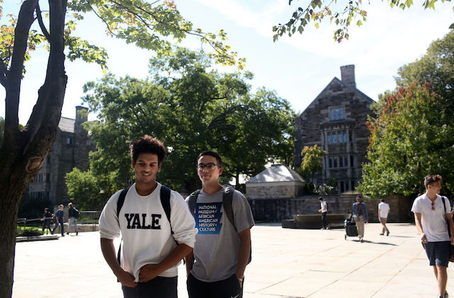 two students, one wearing a Yale sweatshirt, stand on the Yale campus. 