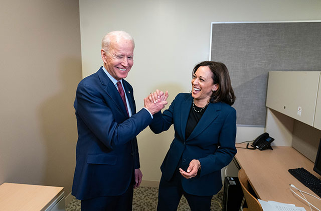 Joe Biden and Kamala Harris. Older white man with gray hair wearing blue suit hi-fiving Black woman wearing blue suit.