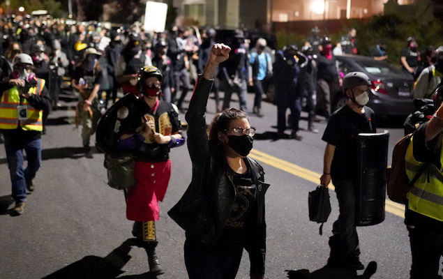 A large group of protesters march in the street, one hold a fist in the air.