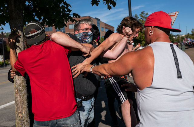 A small group of Black people and White people appear to be in a shoving match while standing outside.
