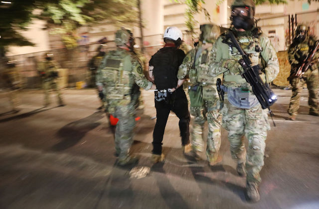federal agents in riot gear arrest a citizen and walk away from the camera,