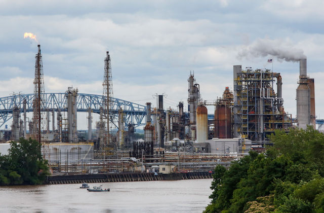 View across a bridge of an oil refinery with smoke coming out of stacks.