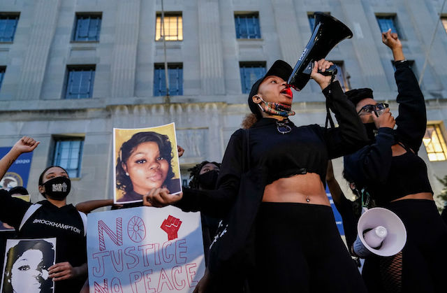 One woman holds a mega-phone in her hand as members of the surrounding crowd hold images of Breonna Taylor