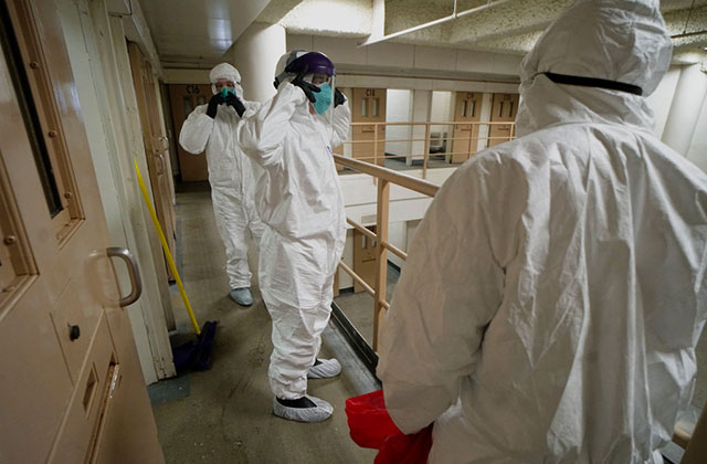 COVID19 Prisons. Men wearing white hazmat suits cleaning a prison cell.