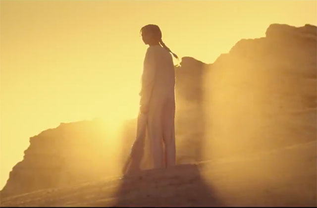Dune. Film shot of a woman standing the bright sunlight on sand dunes.