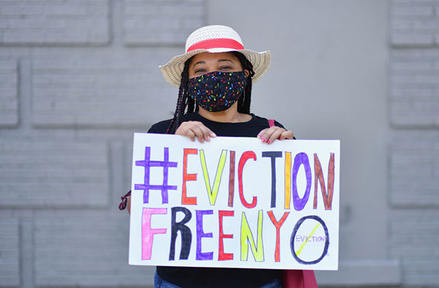 Eviction Protest. Young woman wearing a hat and black face mask holds colorful sign reading: #EvictionFreeNYC