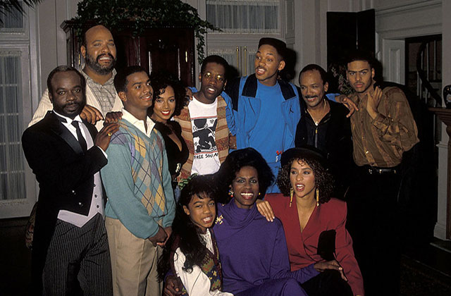 Fresh Prince of Bel Air cast. A group of Black men and women of all ages huddle for a group photo inside of a house.