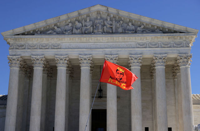 The Supreme Court stands in the background as a red flag with a drawing of Justice Ruth Bader Ginsberg and the words Notorious RBG flies in the foreground.