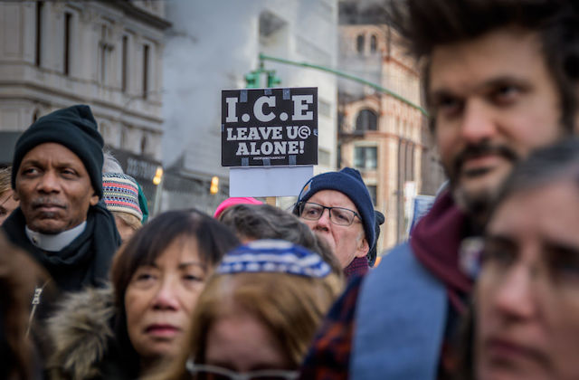 A group of people stand in a group and one person holds up a sign that reads I.C.E. Leave Us Alone