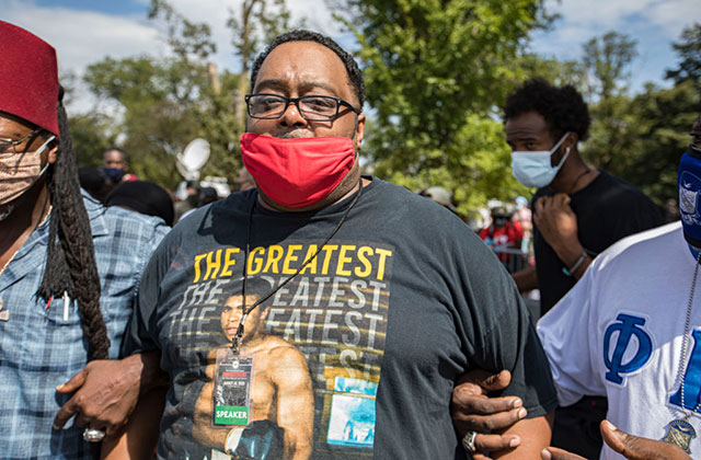 Jacob Blake Sr. Black man with short dark hair and glasses wearing red face mask and black Tee with Muhammed Ali in a boxing stance.