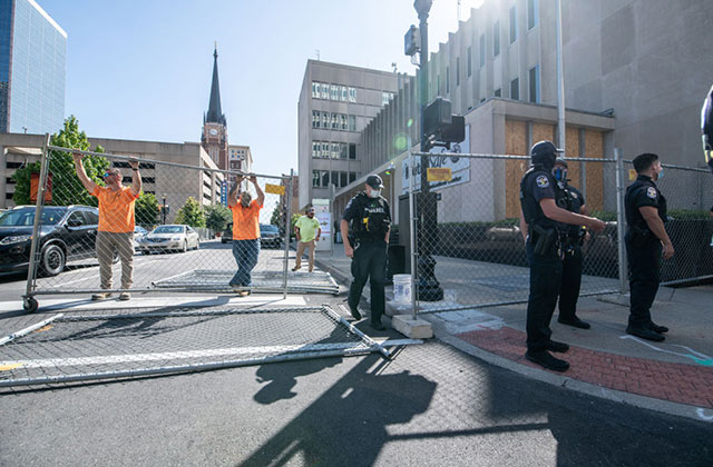 LMPD. Men in police uniforms and construction outfits erect fencing on a street.