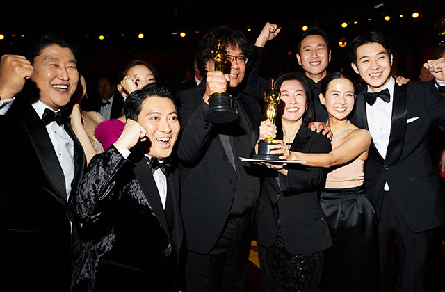 Parasite. Group of Korean men and women dressed in formal black attire holding an Oscar award and cheering.