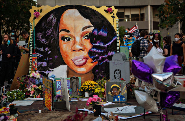 painting of Black woman with long black hair is surrounded by flowers and other tributes.