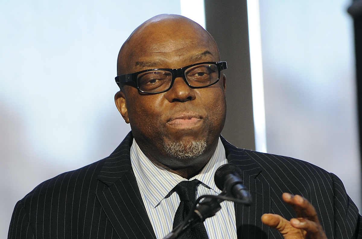 Image of bald, bespectacled Black man speaking at microphone