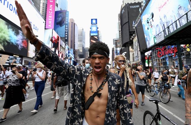Black man raises his arm in protest while marching with a large group through the streets of New York City.