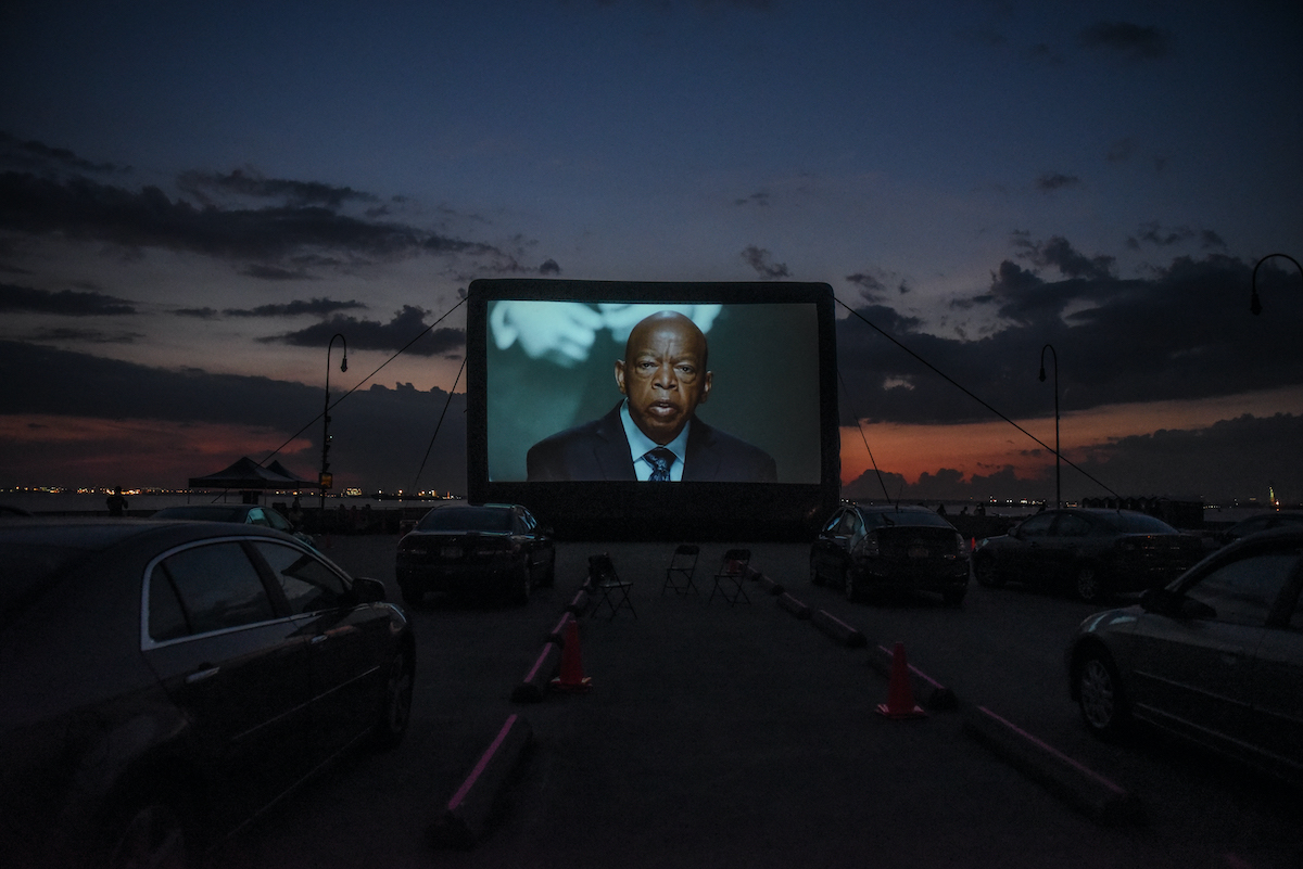 John Lewis. Image of bald, elderly Black man on giant outdoor screen.