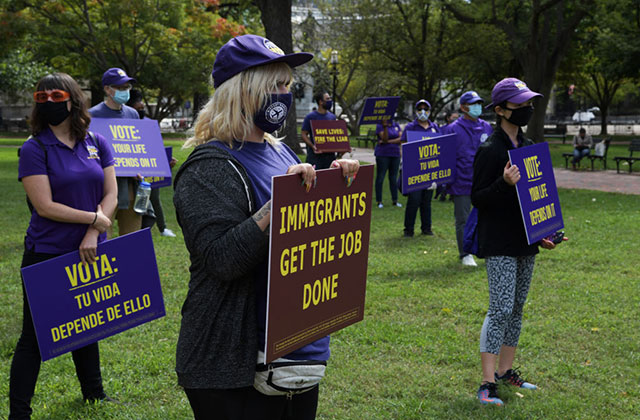 Service Employee International Union. People wearing purple shirts, masks, hats holding signs on a lawn as they socially distance.