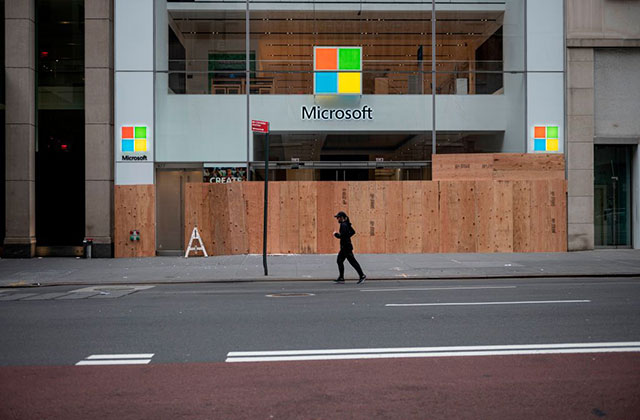 Microsoft. Boarded up storefront with windows logo  and person wearing all black running by.