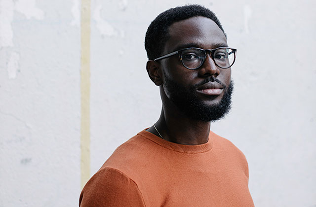 Saidu Tejan-Thomas Jr. Black man with short dark hair, glasses wearing an orange shirt.