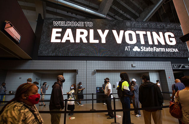 Voting. A line of Black people form a line inside of a rope under a huge sign reading Early Voting.
