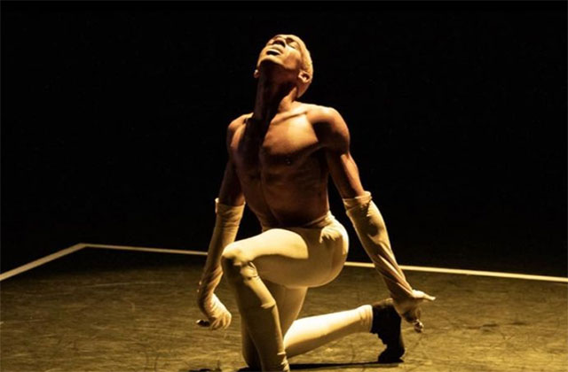 Black Magic. Shirtless Black man wearing yellow tights and black shoes on one knee.