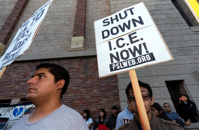 A black and white protest sign reads, Shut Down I.C.E. Now!