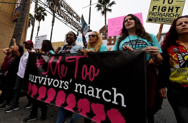 a group of women wearing blue shirts stand in a row and hold a large banner that reads, Me Too Survivors March