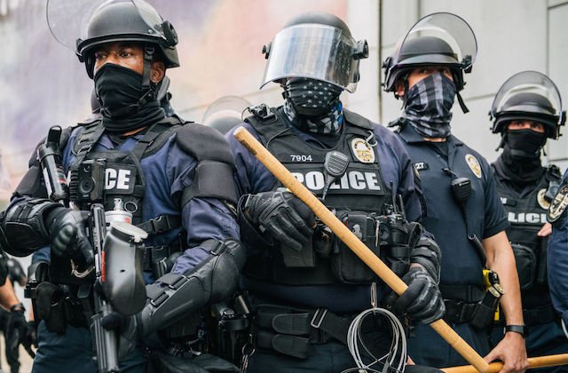 Fout uniformed police officers in riot gear stand closely together.