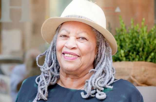 Brown skinned, older woman with white locs and a straw hat on top, smiling