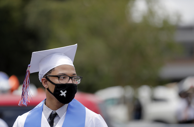 A student in a graduation cap and gown dons a mask with their stole during the COVID-19 pandemic.