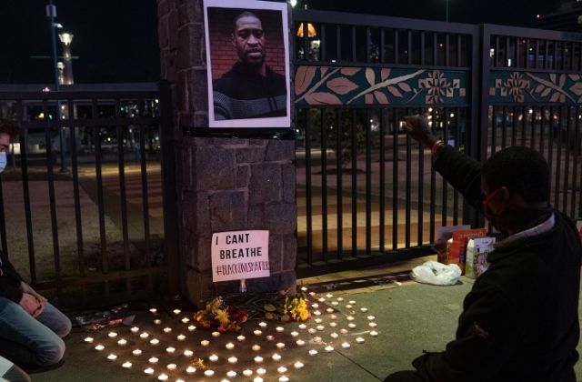 Protesters sit in front of a candlelit vigil for George Floyd