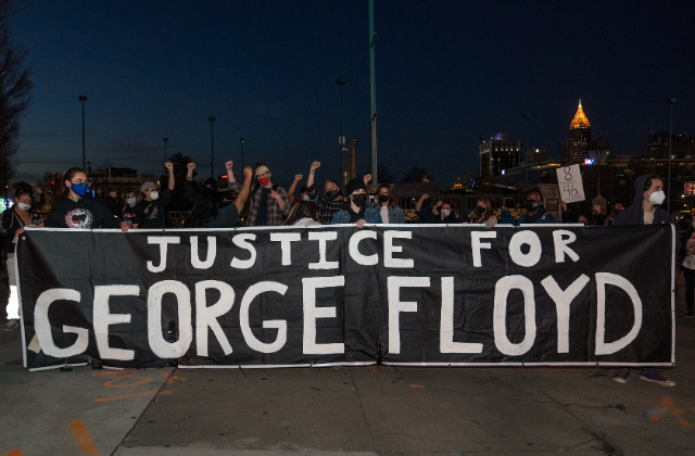Protesters hold a sign that reads "Justice for George Floyd".