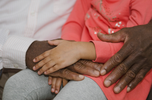 A close-up photo of hands as a Black child sits on their grandparent's lap.