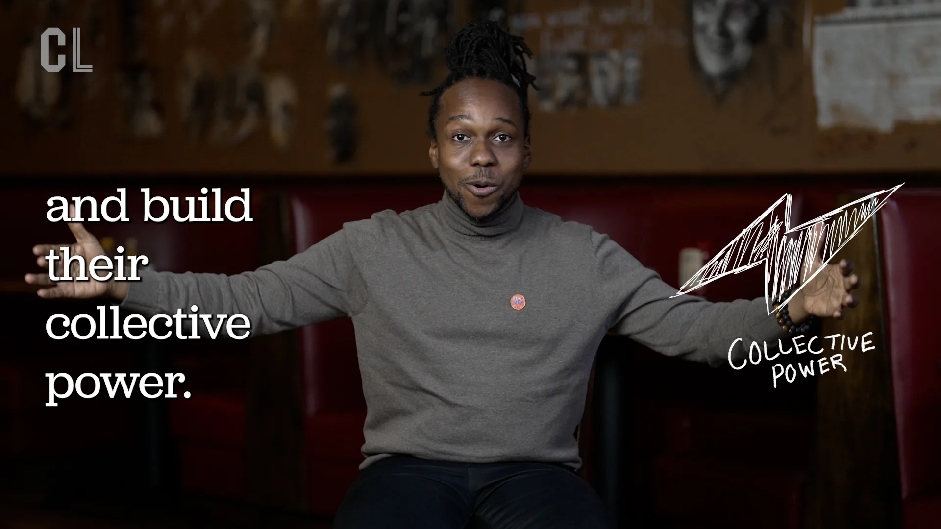 A person wearing a gray turtleneck shift with their arms outstretched sitting in a chair facing the camera.