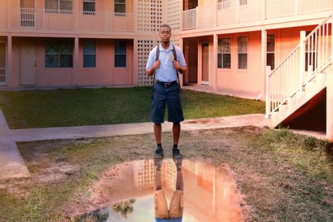 David, dressed in his school uniform, stands in front of a big puddle in the middle of his housing project 