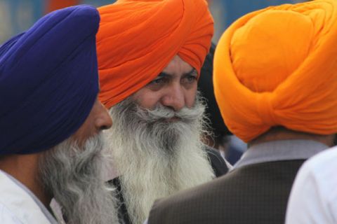 People in blue, orange and yellow turbans with long beards look into the distance.