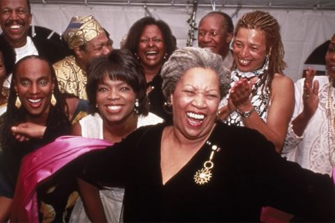 Toni Morrison. Older Black woman with gray locs pulled back wearing black top and surrounded by clapping Black women.