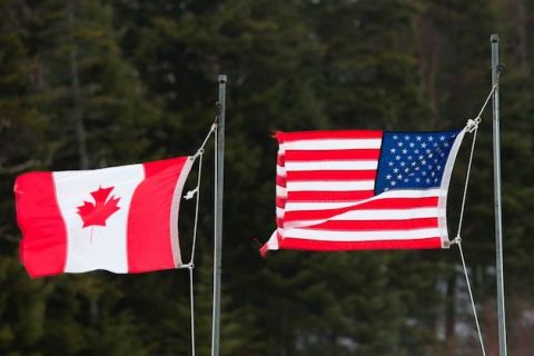 Red and white Canadian flag and red, white and blue American flag fly next to each other at the U.S.-Canada border.