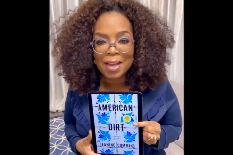 Oprah Winfrey. Black woman with shoulder length brown hair wearing glasses and blue top holding an electric reader showing "American Dirt" book cover.