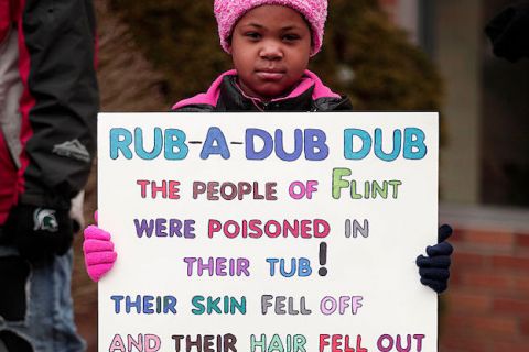 Young Black girl wearing a pink hat and matching pink coat holds a sign protesting the Flint water crisis in Flint, Michigan.
