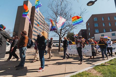 People walking carrying transgender and LGBTQ flags.